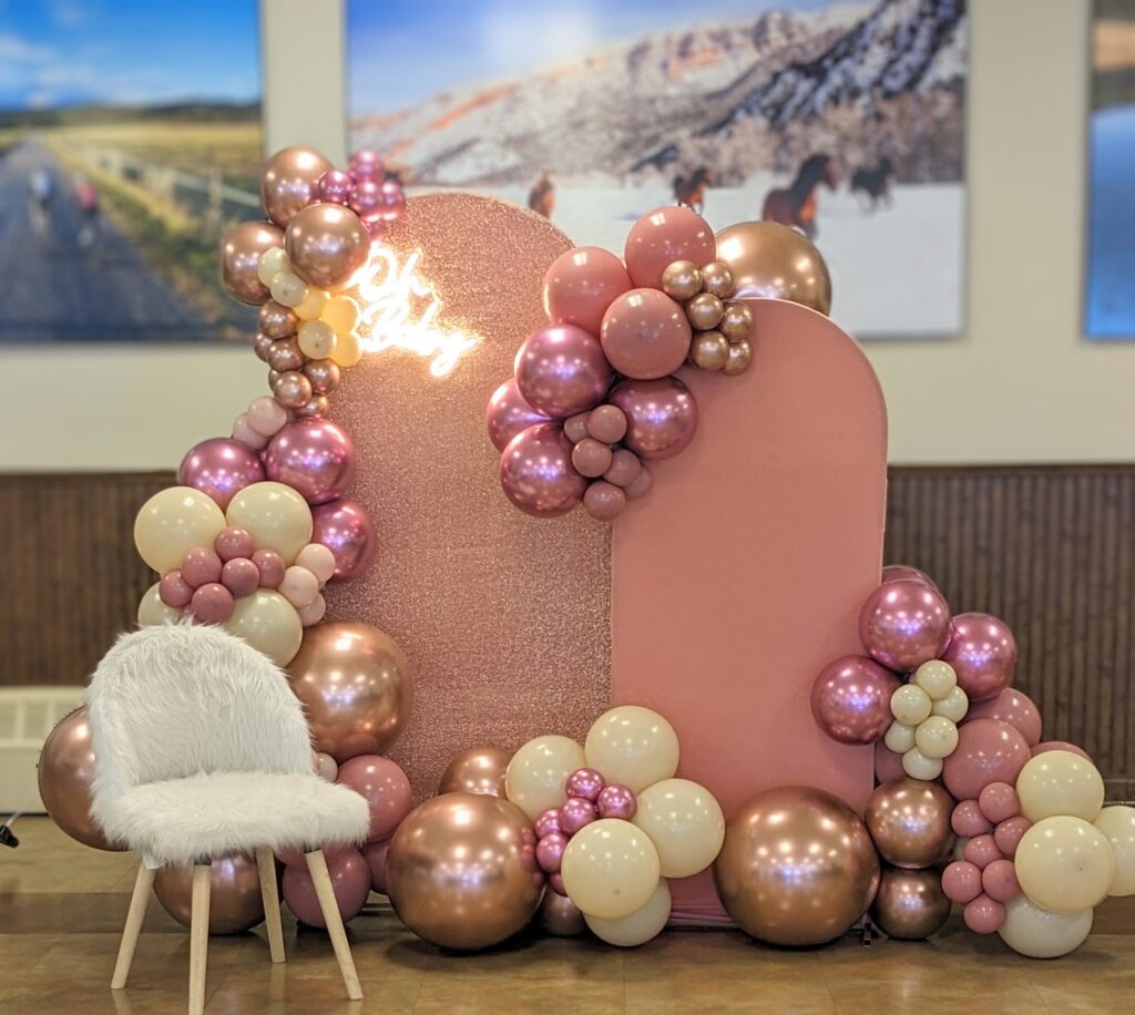 The Fluffy Stuff baby shower photo setup with pink background, neon light says "Oh Baby" with a white fuzzy chair and pink, rose gold, and cream colored balloons